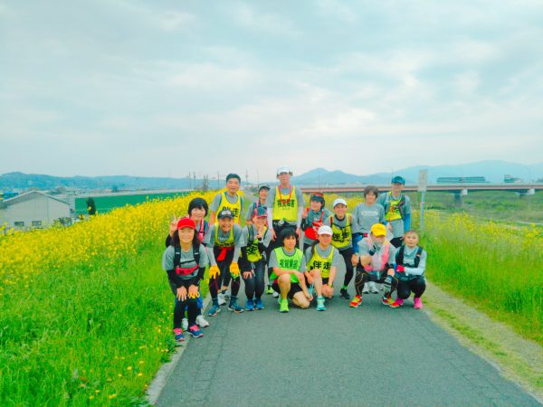 にじょうざんを背景に大和川の堤防で記念撮影、両側の河川敷は菜の花でいっぱい、まっ黄色