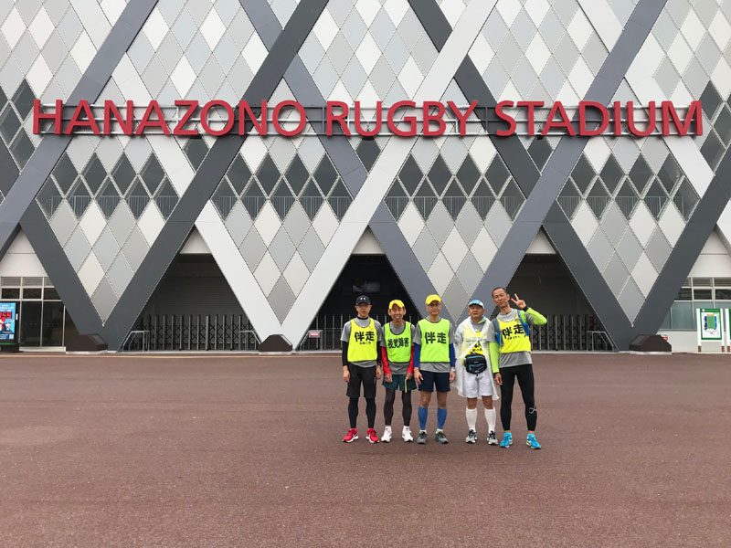 「HANAZONO RAGBY STADIUM」とかいてある競技場壁面を背景に５人並んでパシャ