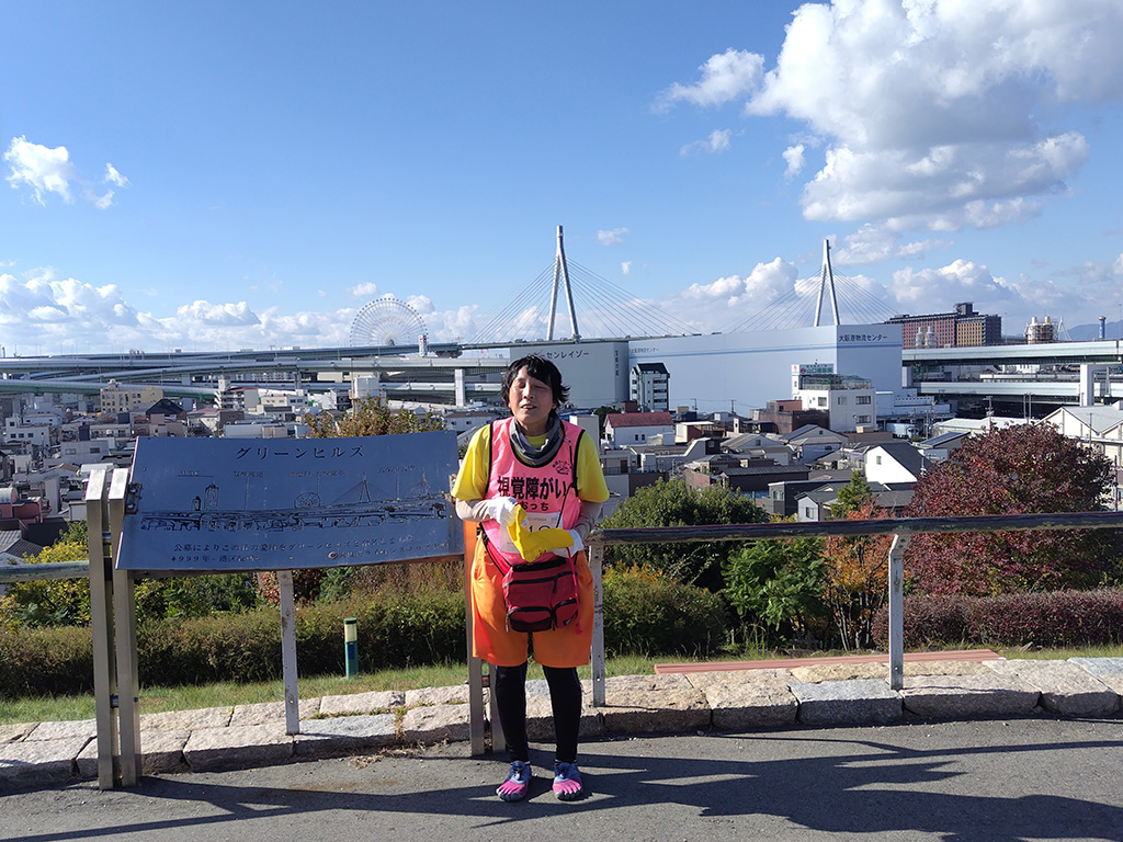 グリーンヒルス頂上からの眺めを背景にして立つカオッチさん